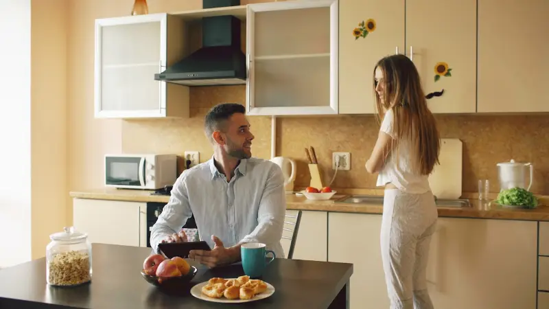 Two people talking together in a shared kitchen in the morning.