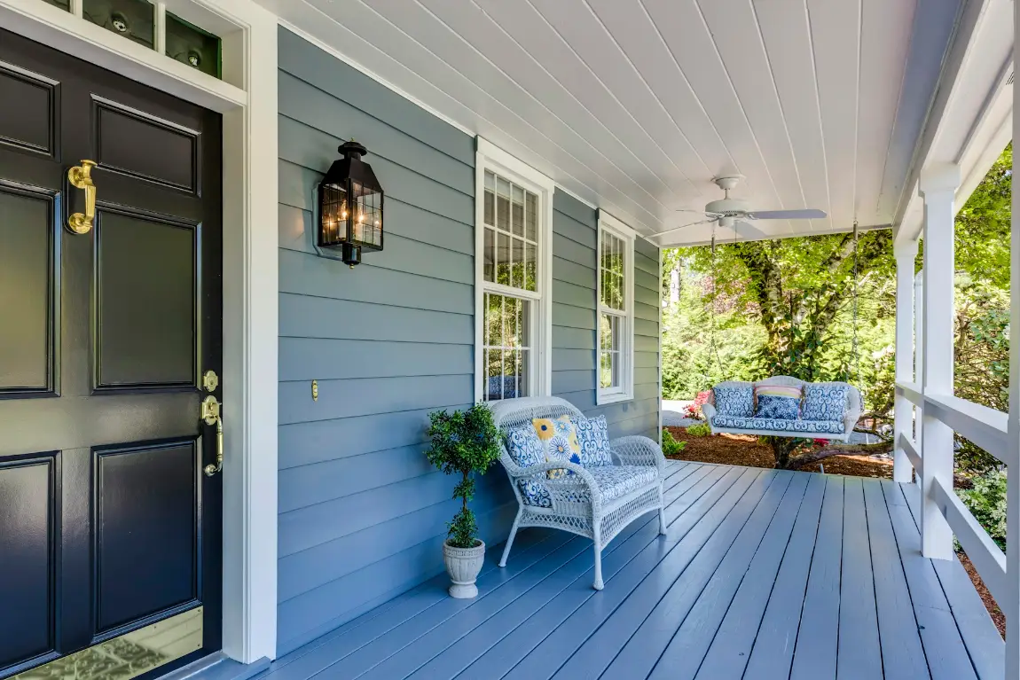 A welcoming front porch with a painted door, wicker seating and a hanging swing.